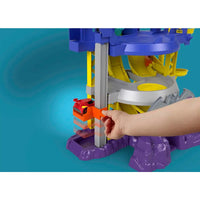 Una mano tiene un’auto hot wheels rosso e arancione vicino all’entrata del playset fisher-price dc batwheels batcaverna lancia e sfreccia