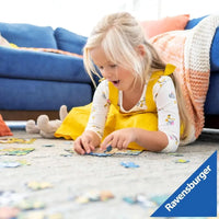 Una ragazza giovane in abito giallo floreale assemblea un puzzle ravensburger demon hunters xxl 100 pezzi